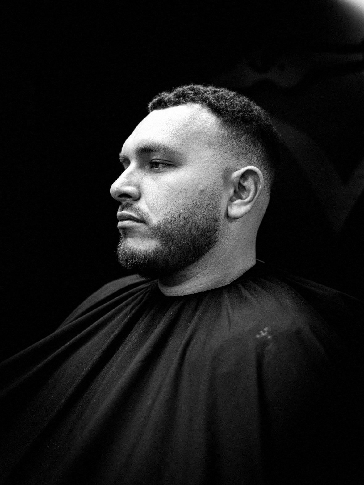 Black-and-white portrait of Alex Kirk wearing a barber cape
