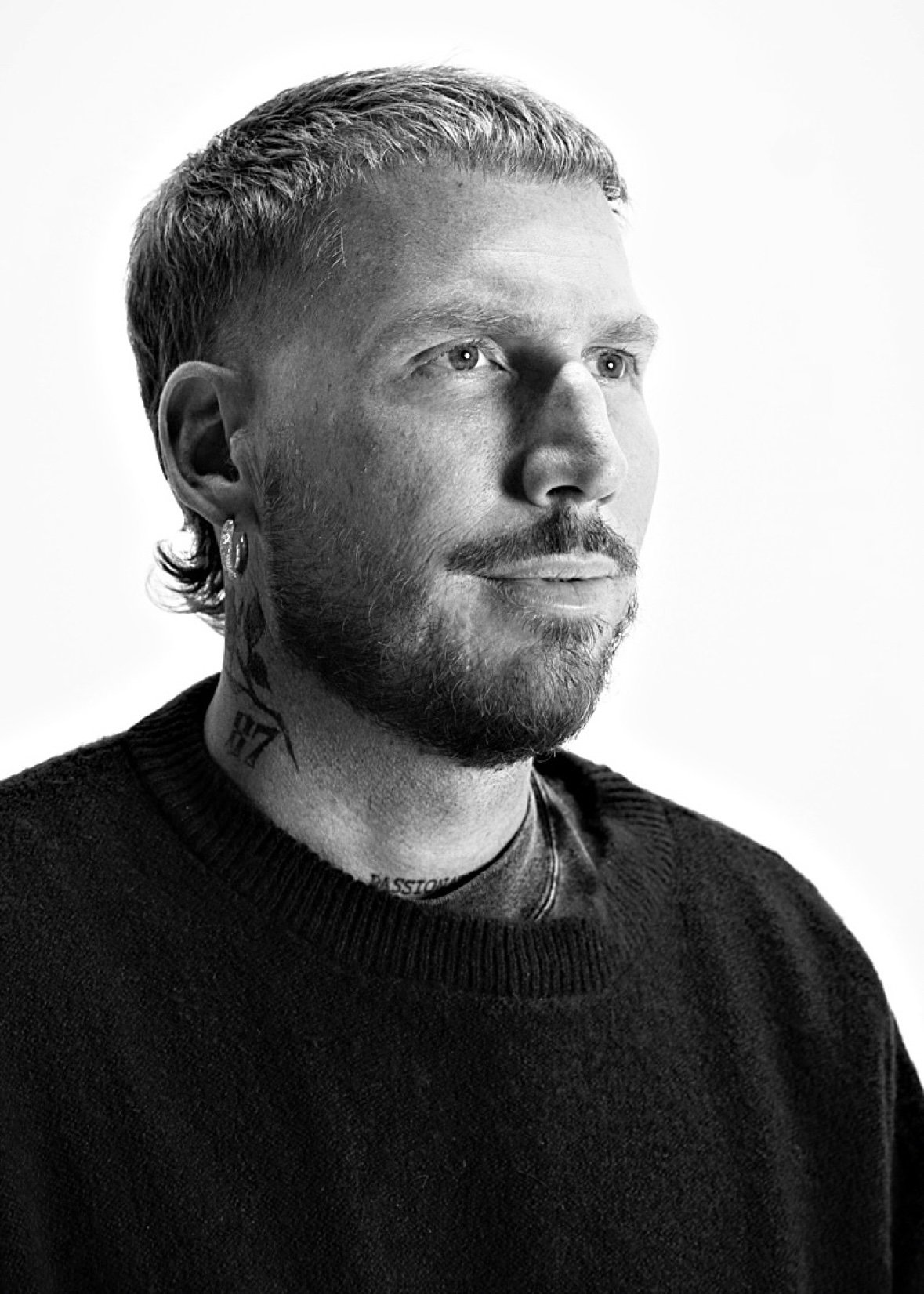 Black-and-white editorial portrait of a man with a textured crop and beard wearing a black sweater