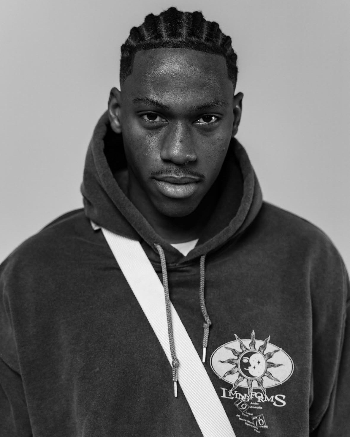 Black-and-white portrait of Jonathon David with cornrows wearing a graphic hoodie